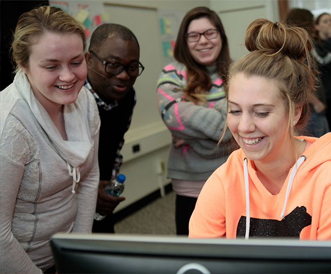 Students around a computer screen smiling